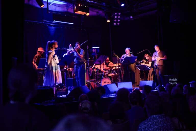 A group of musicians play on stage under purple light.